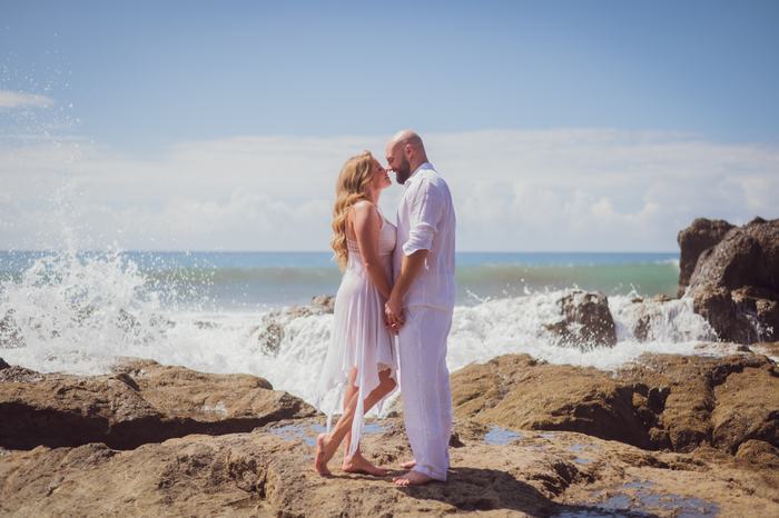 Pamela and Tanner nose to nose as a wave breaks behind them