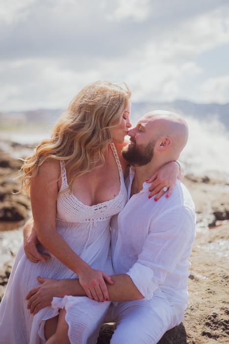 Pamela and Tanner kissing, seated on the rocks