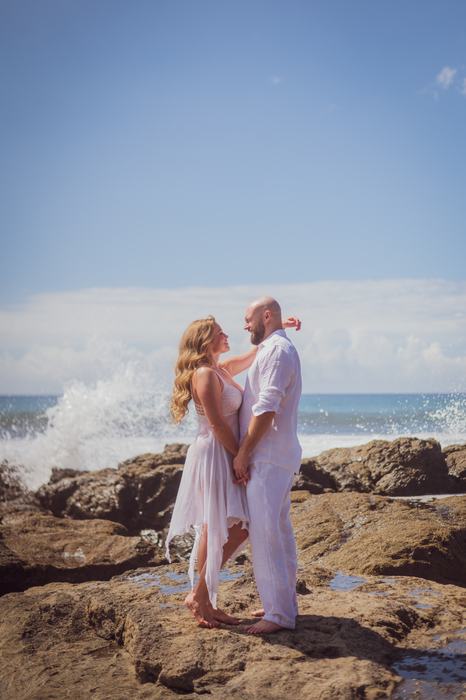 Pamela and Tanner embracing on the rocks as spray rises