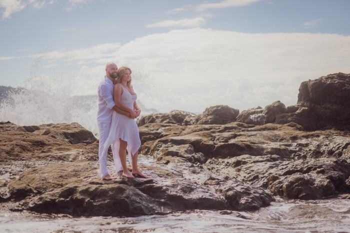 Pamela and Tanner on the rocks with a wave crashing behind